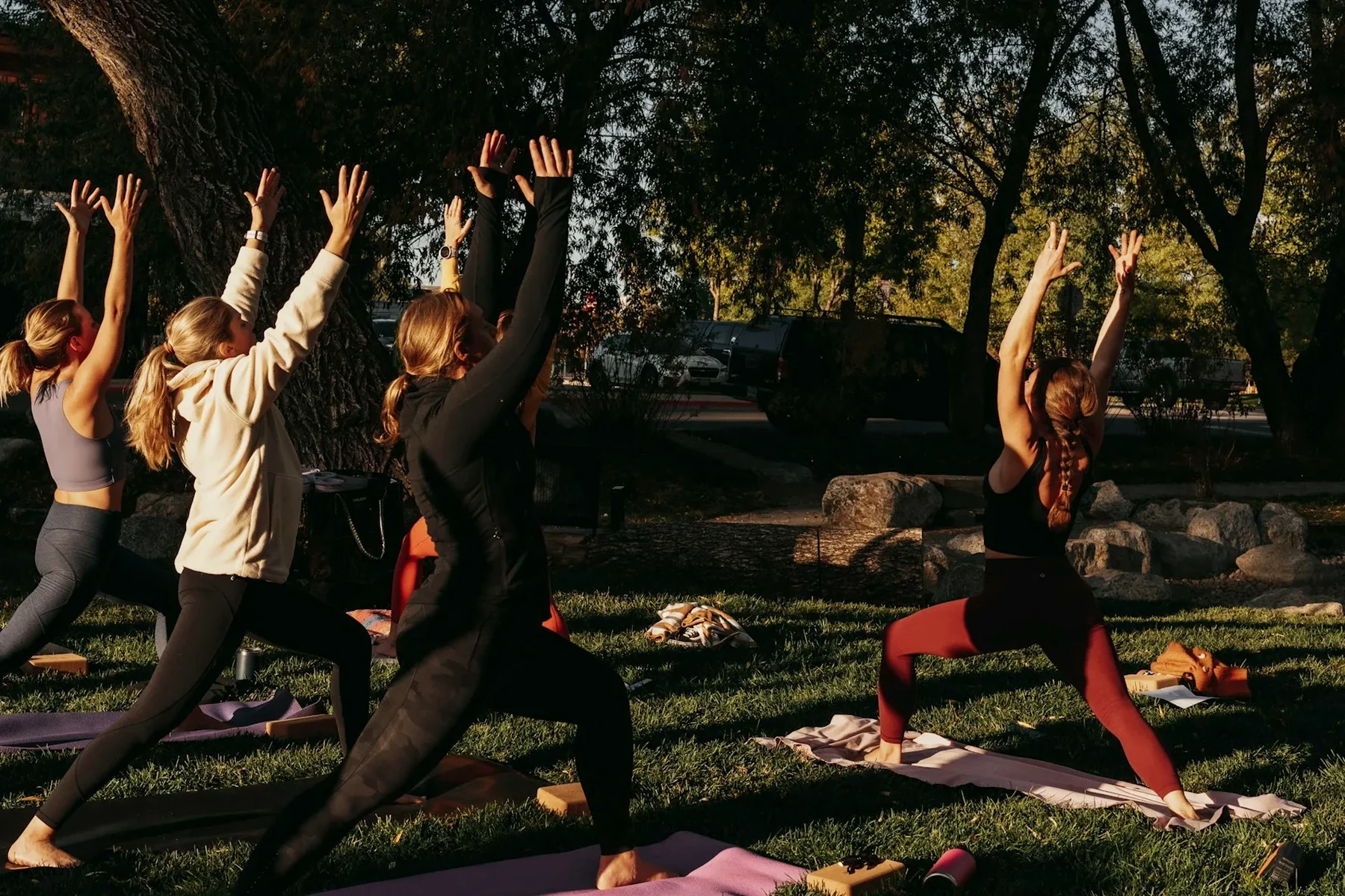 Cours collectif de yoga en plein air dans un parc, avec tapis et professeur devant le groupe